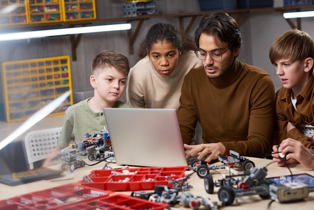 children and man working on computer and robotics equipment