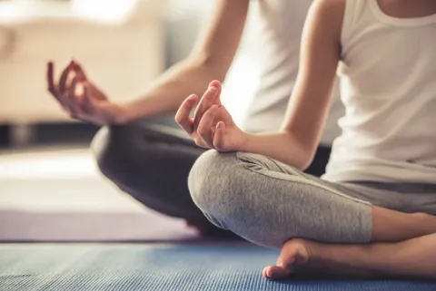 Two people in a yoga pose while sitting on yoga mats on the floor