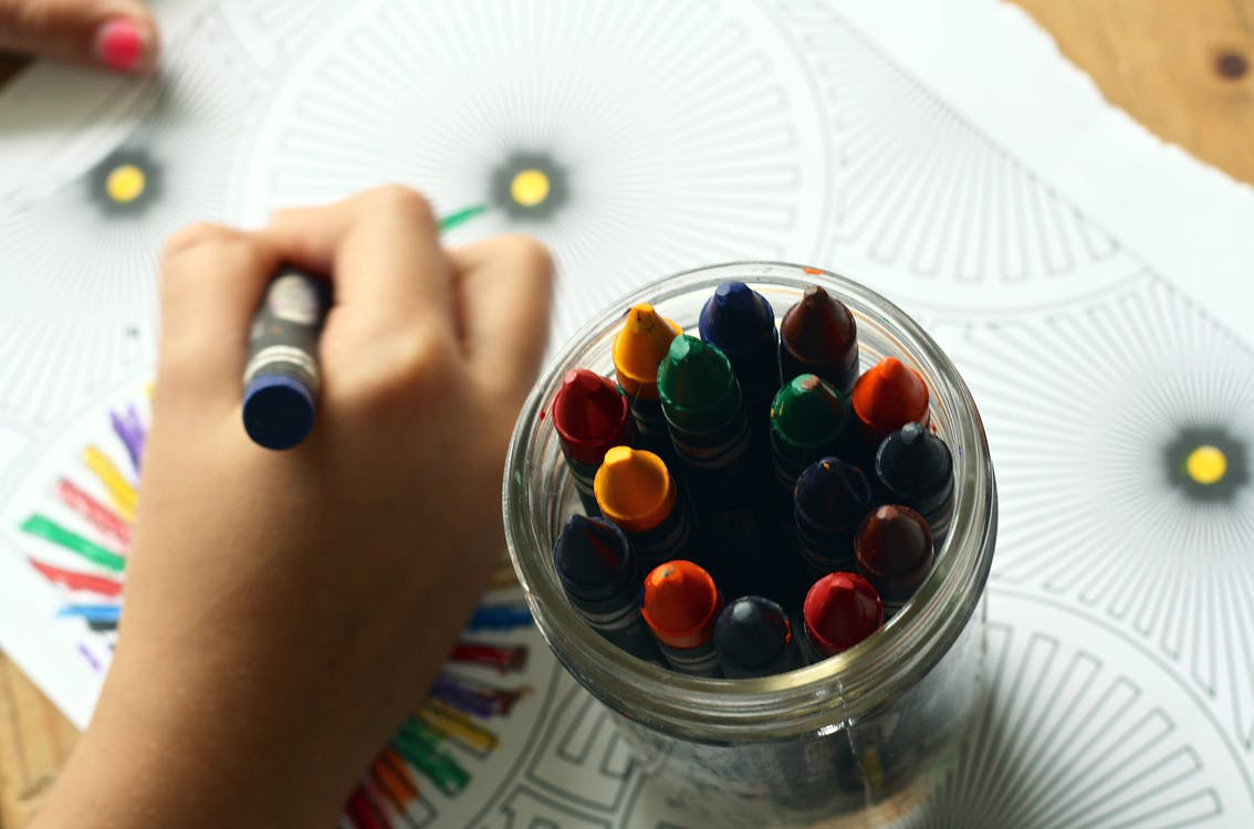 Hand coloring pages next to a cup of crayons